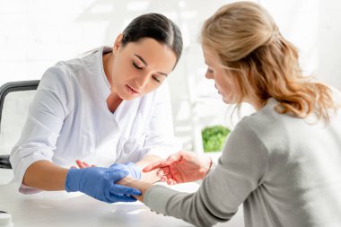 Beyaz önlüklü çekici dermatolog klinikteki hastanın derisini inceliyor.