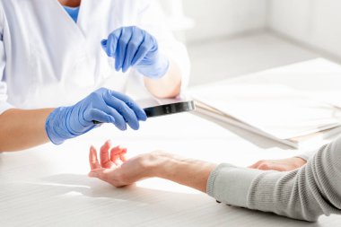 Dermatolojistin klinikte büyüteçle deri incelemesi yapması.