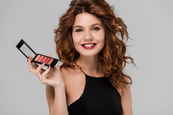 Gelukkig Krullend Vrouw Holding Set Van Lip Gloss Geïsoleerd Grijs — Stockfoto