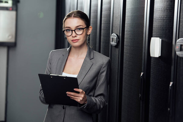 pretty businesswoman in glasses holding clipboard in data center 