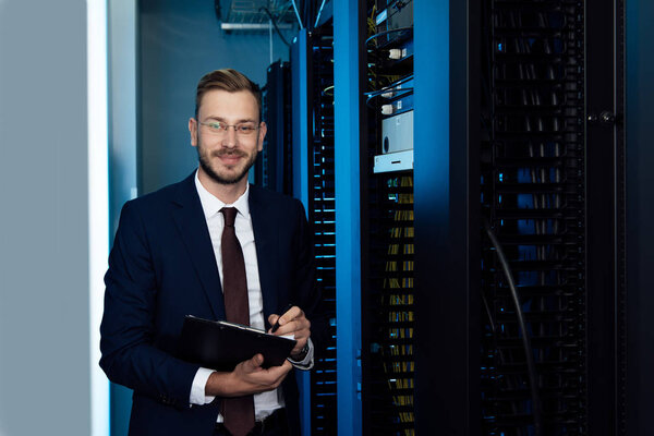 happy businessman in glasses holding clipboard in data center 