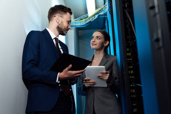 selective focus of happy businesswoman and businessman with clipboard in data center 