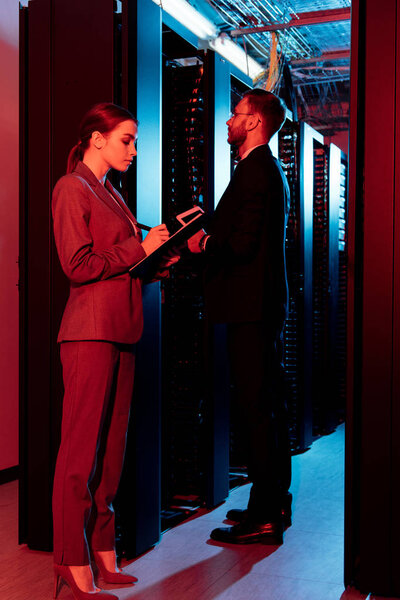attractive businesswoman holding clipboard near businessman in data center 