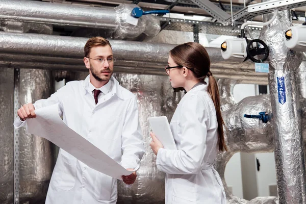 Ingeniero Bata Blanca Mirando Compañero Trabajo Gafas Mientras Sostiene Plano — Foto de Stock