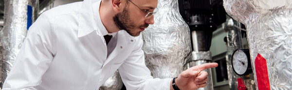 панорамный снимок бородатого инженера в белом халате, держащего цифровой планшет и указывающего пальцем на систему подачи воздуха
 