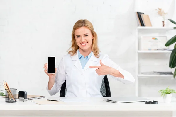 Nutricionista Sorridente Sentado Mesa Apontando Com Dedo Para Smartphone Com — Fotografia de Stock