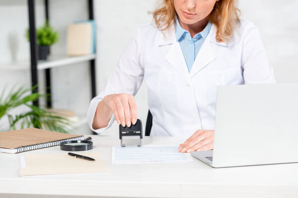 обрезанный вид диетолога, сидящего за столом и штамповки бумаги в клинике
 