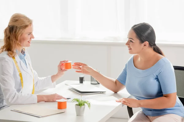 笑顔の栄養士がテーブルに座りヨーグルトをクリニックの患者に与えるという — ストック写真