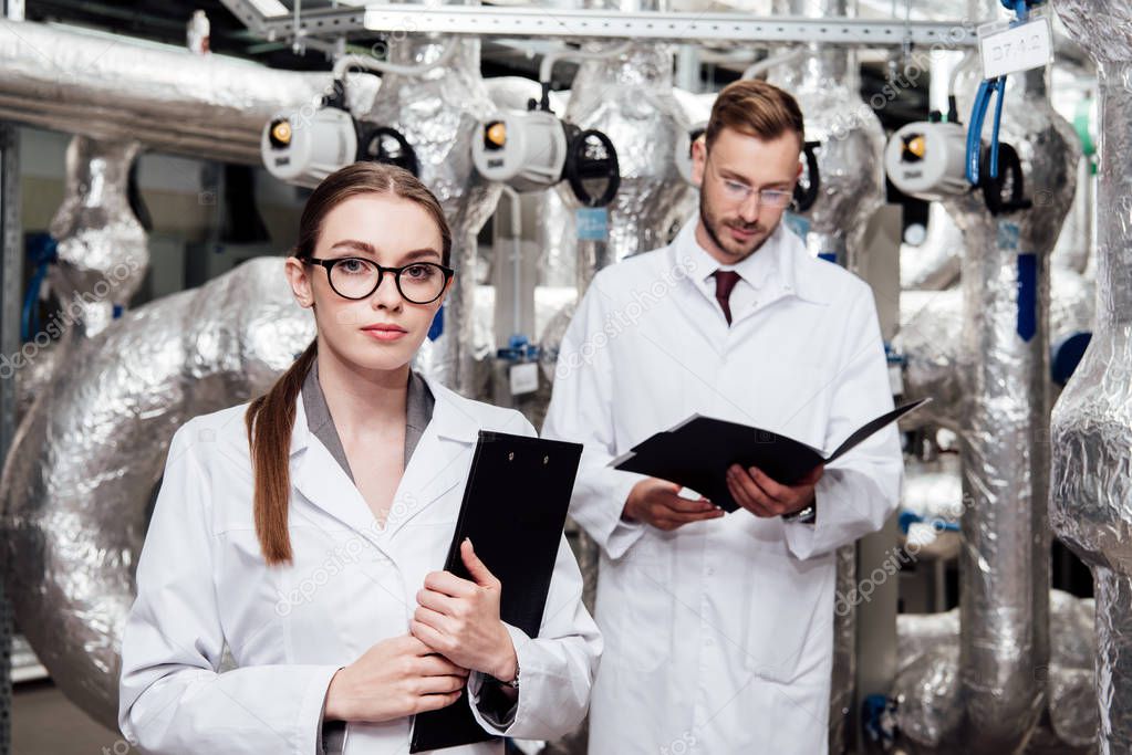 selective focus of attractive engineer holding clipboard near bearded coworker  