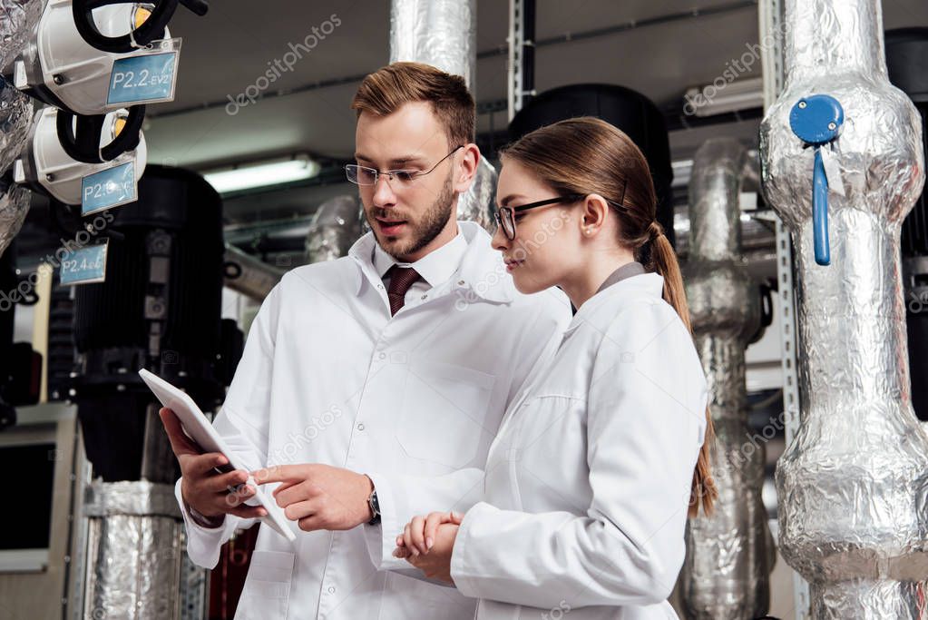 handsome engineer pointing with finger at digital tablet near attractive coworker and air compressor system 