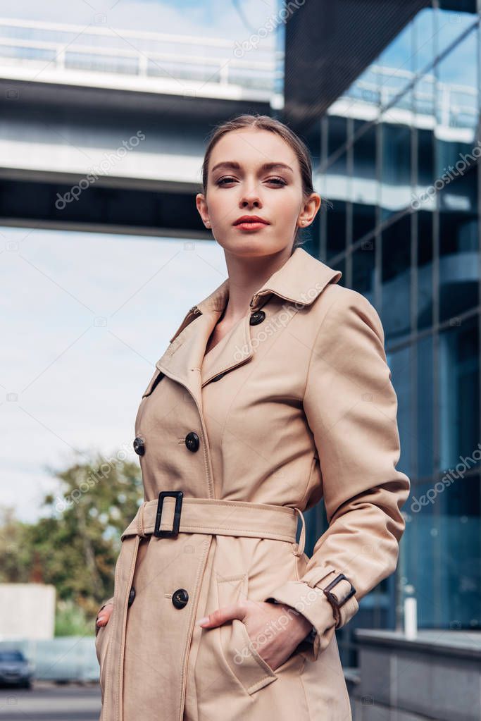 attractive woman in trench coat standing with hands in pockets 