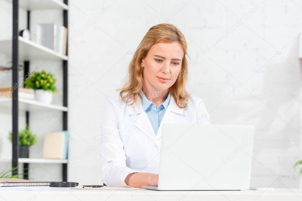 attractive nutritionist sitting at table and using laptop in clinic 