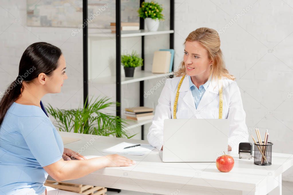smiling nutritionist sitting at table and talking with patient in clinic 