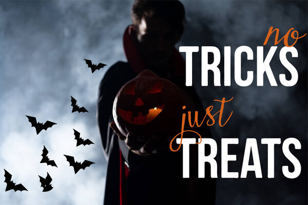 selective focus of man holding pumpkin on black background with smoke and no tricks just treats illustration