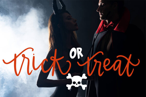 handsome man in cloak looking at girl with horns holding flogging whip on black background with smoke and trick or treat illustration