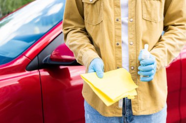 cropped view of young man in latex gloves using antiseptic and rag for cleaning car during coronavirus pandemic clipart