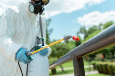 selective focus of specialist in hazmat suit and respirator disinfecting sports ground in park during covid-19 pandemic clipart