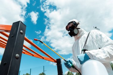 professional specialist in hazmat suit and respirator disinfecting sports ground in park during covid-19 pandemic clipart