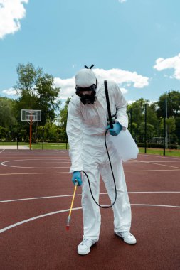 Tehlikeli madde giysisi ve solunum cihazıyla çalışan işçiler covid-19 salgını sırasında parkta basketbol sahasını dezenfekte ediyorlar.