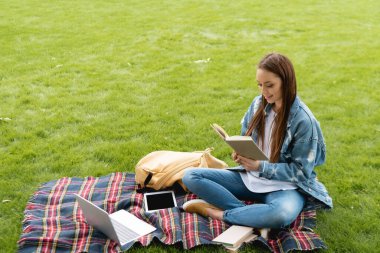 Mutlu ve çekici öğrenci aletlerin yanında kitap okuyor, online çalışma konsepti 