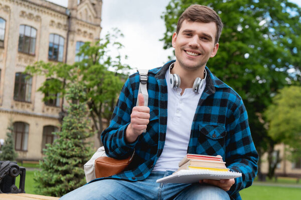 cheerful student showing thumb up and holding books 
