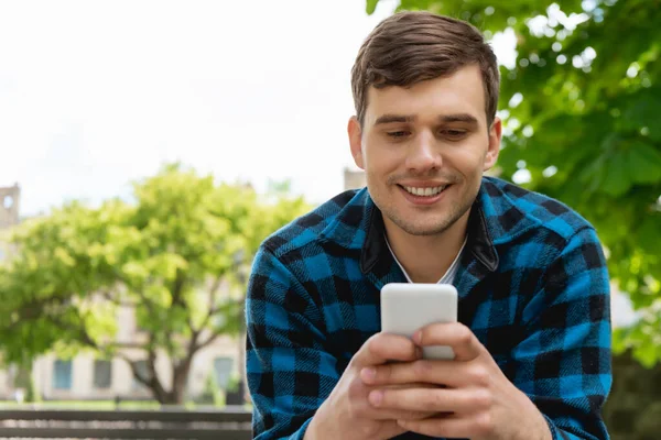 Estudiante Guapo Sonriendo Mientras Usa Teléfono Inteligente — Foto de Stock