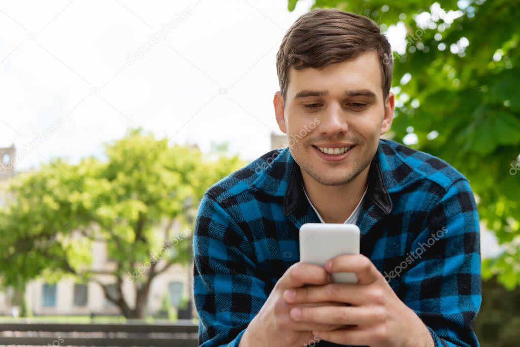 handsome student smiling while using smartphone 