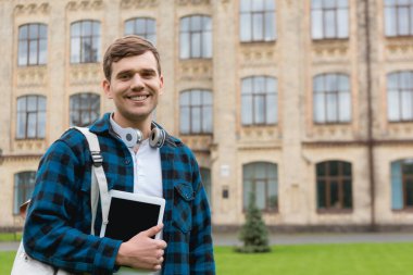cheerful man holding digital tablet with blank screen while standing near university campus clipart