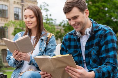 Dışarıda kitap okuyan mutlu ve genç öğrencilerin seçici odağı.