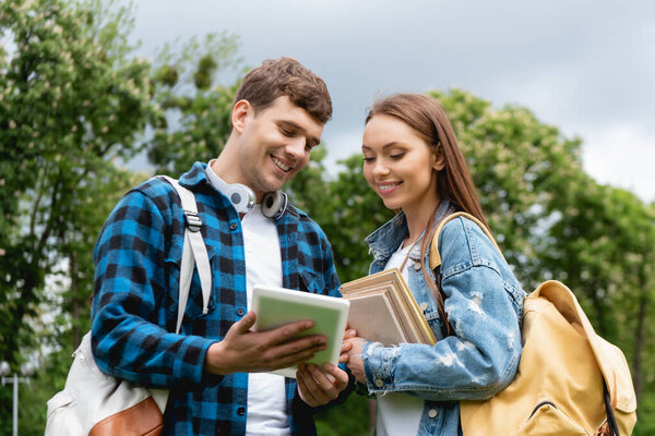 cheerful students with backpacks and books looking at digital tablet 