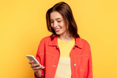 Sarıda izole edilmiş akıllı telefon kullanan mutlu genç bir kadın. 