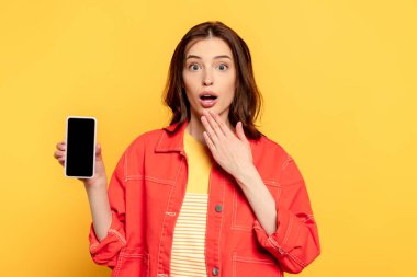 Sarı ekranda boş ekranlı akıllı telefonu tutan genç bir kadın şaşırdı. 
