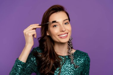happy woman holding eyebrow brush while styling eyebrow isolated on purple clipart
