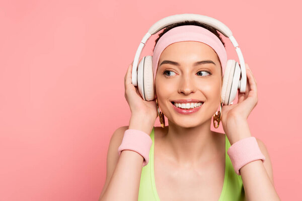 веселая женщина касается наушников, слушая музыку изолированы на розовый
 