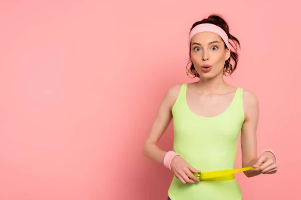 surprised woman with headband touching belt on bodysuit on pink