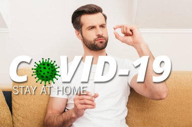 Evdeki kanepede hap ve bir bardak su tutan düşünceli bir adam, covid-19 illüstrasyon