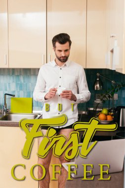 Külotlu ve gömlekli yakışıklı adamın mutfakta kahve içerken dizüstü bilgisayara baktığı seçici odak noktası.