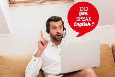 Selective focus of excited freelancer in headset showing idea gesture during video chat on laptop at home, do you speak English illustration clipart