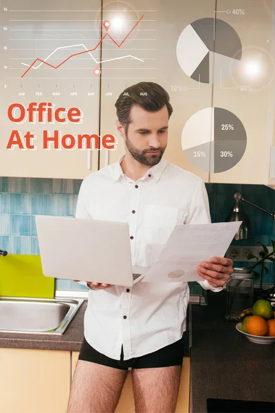 穿着衬衫和内裤的英俊男人一边拿着笔记本电脑一边在厨房里做文档工作 办公室里的插图 — 图库照片