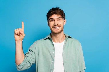 happy man looking at camera while showing idea gesture on blue clipart