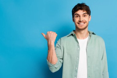 Mutlu genç adam mavi kameraya bakarken başparmağıyla işaret ediyor.