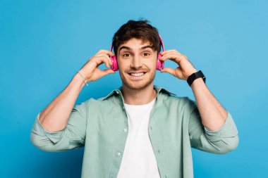 Mutlu genç adam mavi kanalda müzik dinlerken kablosuz kulaklıklara dokunuyor.