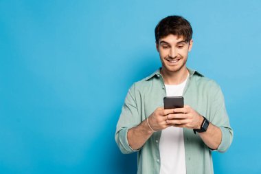 Neşeli genç adam mavi telefonda akıllı telefonla konuşuyor.