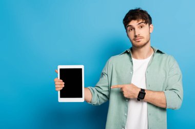 Yakışıklı genç adam mavi ekranlı dijital tableti işaret ediyor.