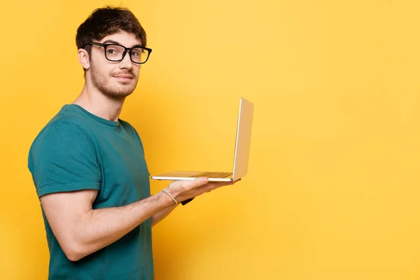 Sonriente Joven Mirando Cámara Mientras Sostiene Ordenador Portátil Amarillo — Foto de Stock