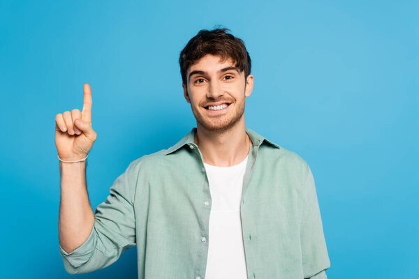 happy man looking at camera while showing idea gesture on blue