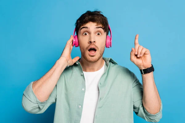 Shocked Young Man Touching Wireless Headphones Showing Idea Gesture Blue — Stock Photo, Image