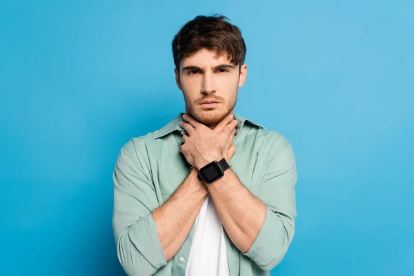 Dissatisfied Young Man Touching Neck While Looking Camera Blue — Stock Photo, Image