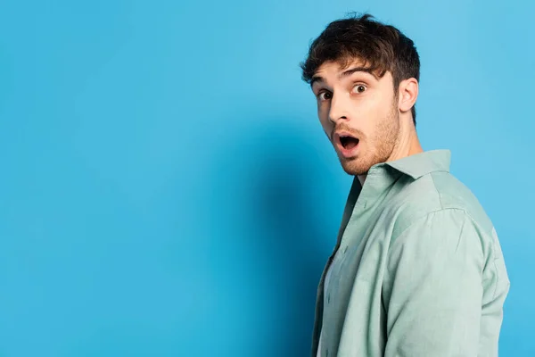 shocked young man with open mouth looking at camera on blue