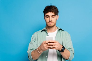ciddi genç adam mavi telefondan izole edilmiş akıllı telefonda sohbet ediyor.